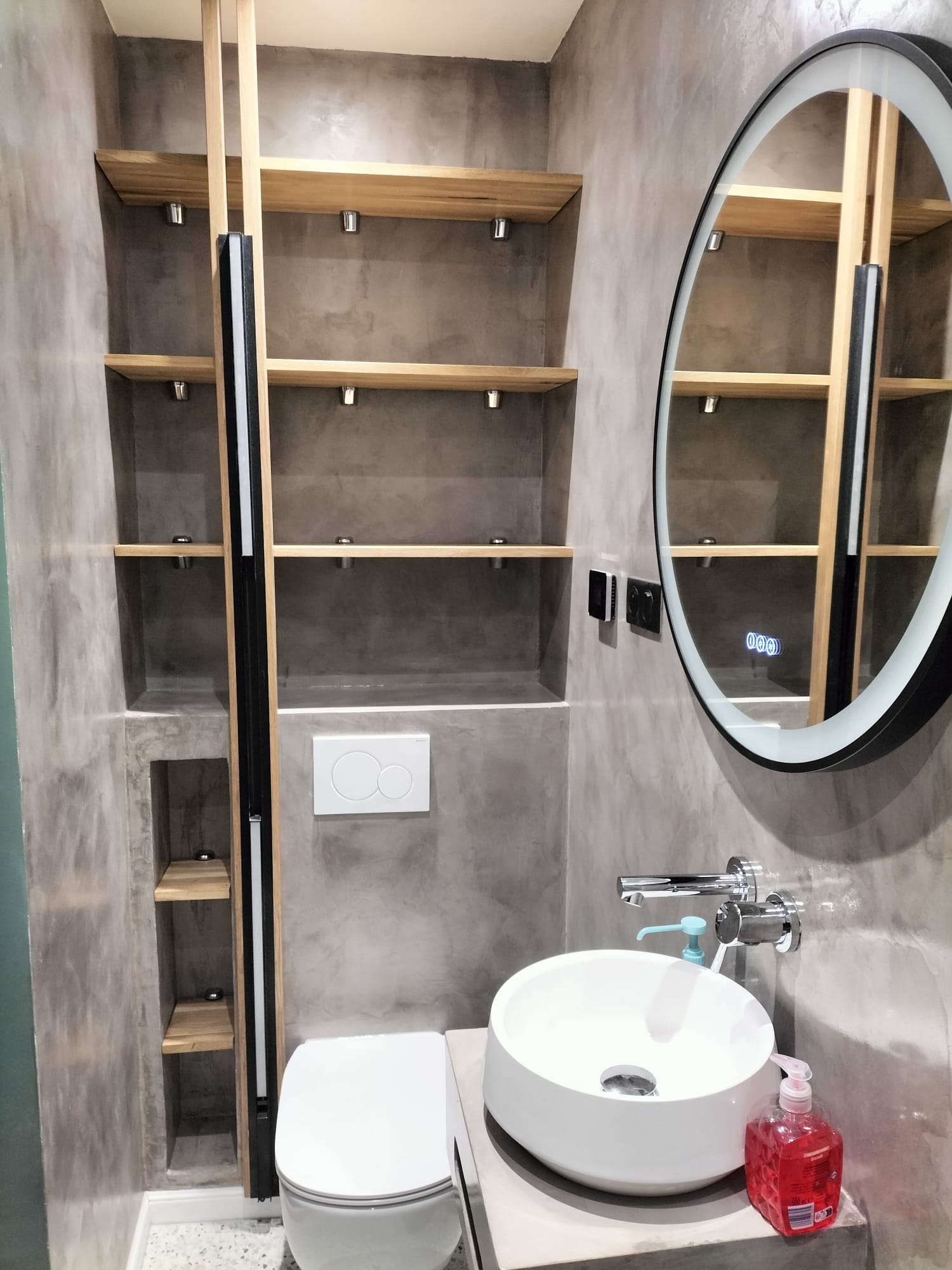 salle de bain avec meuble lavabo, étagères et miroir rond